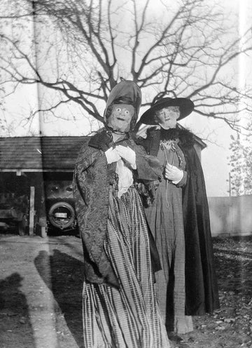 Vintage black and white photo of two people in eerie Halloween costumes with masks and old-fashioned clothing outdoors