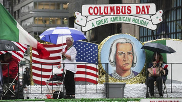 Columbus Day parade float with large Columbus portrait, American and Italian flags, people holding umbrellas in rain