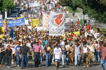 Large diverse crowd marching in a protest with signs supporting American Indian Movement and social justice