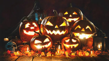 Glowing carved Halloween pumpkins with candles, autumn leaves, skull, and lanterns on wooden surface