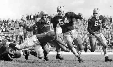 Black and white vintage American football game with players in leather helmets and numbered jerseys running on field