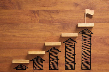 Wooden blocks arranged as ascending steps on a wooden surface with drawn arrows and a flag representing success milestones