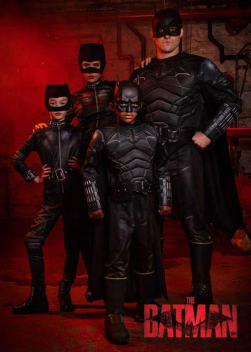 Family of four in detailed black Batman and Catwoman Halloween costumes against a red background with The Batman logo