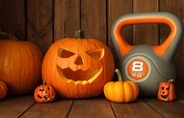 Carved Halloween pumpkin jack-o'-lantern with small pumpkins and 8 kg kettlebell on wooden floor